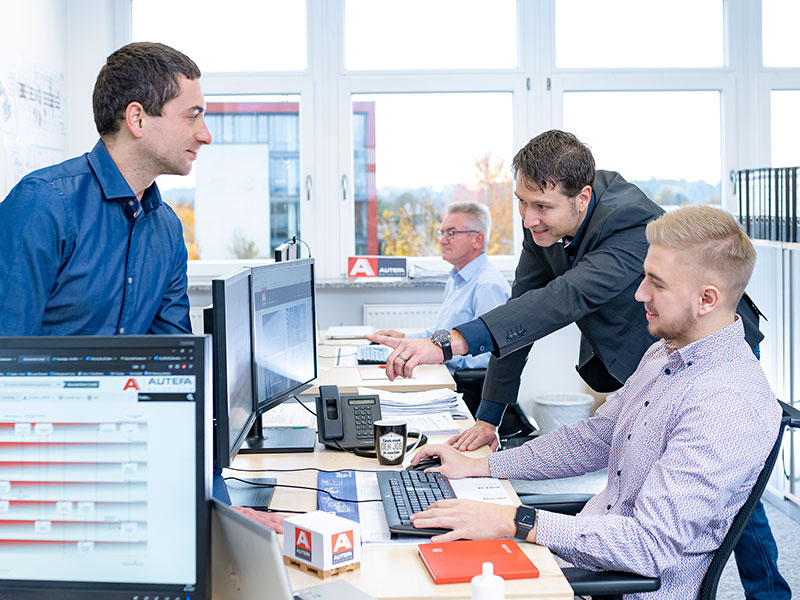 Quality management team discusses in front of a computer