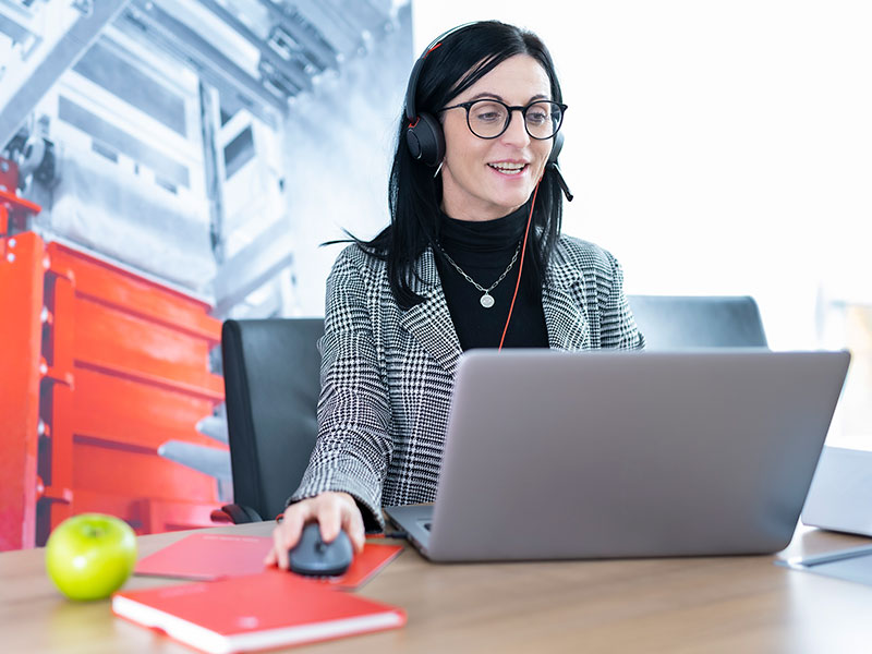 Woman smiles while working on a laptop and talking on her headset